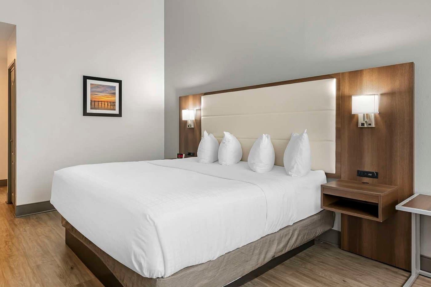 A king guest room at the Best Western Plus First Coast Inn & Suites, with a padded headboard, bedside reading lights, and wood-look flooring