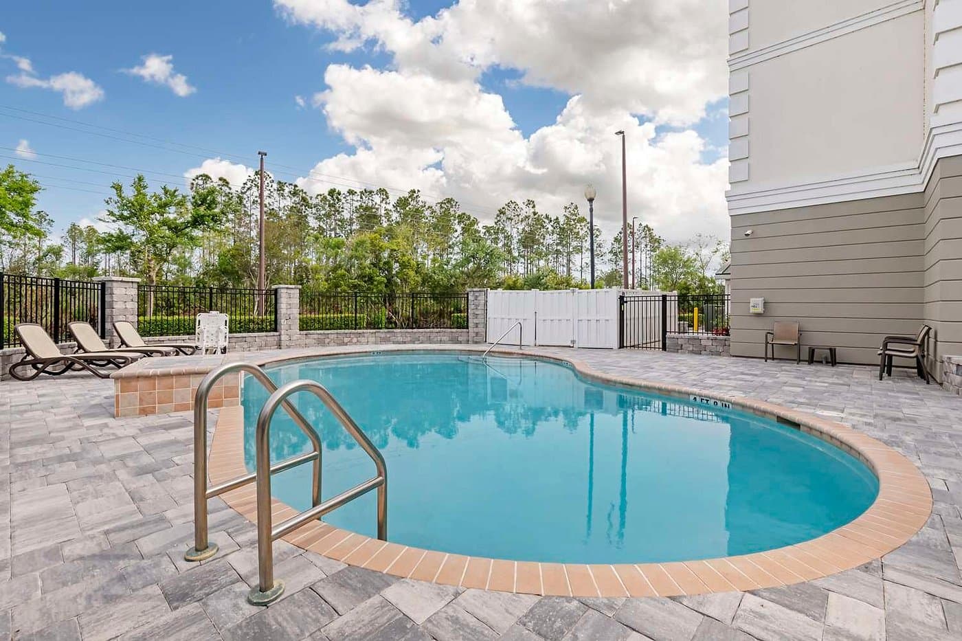 The outdoor pool at the Best Western Plus First Coast Inn & Suites, ringed by a paver deck with lounge chairs under a partly cloudy sky