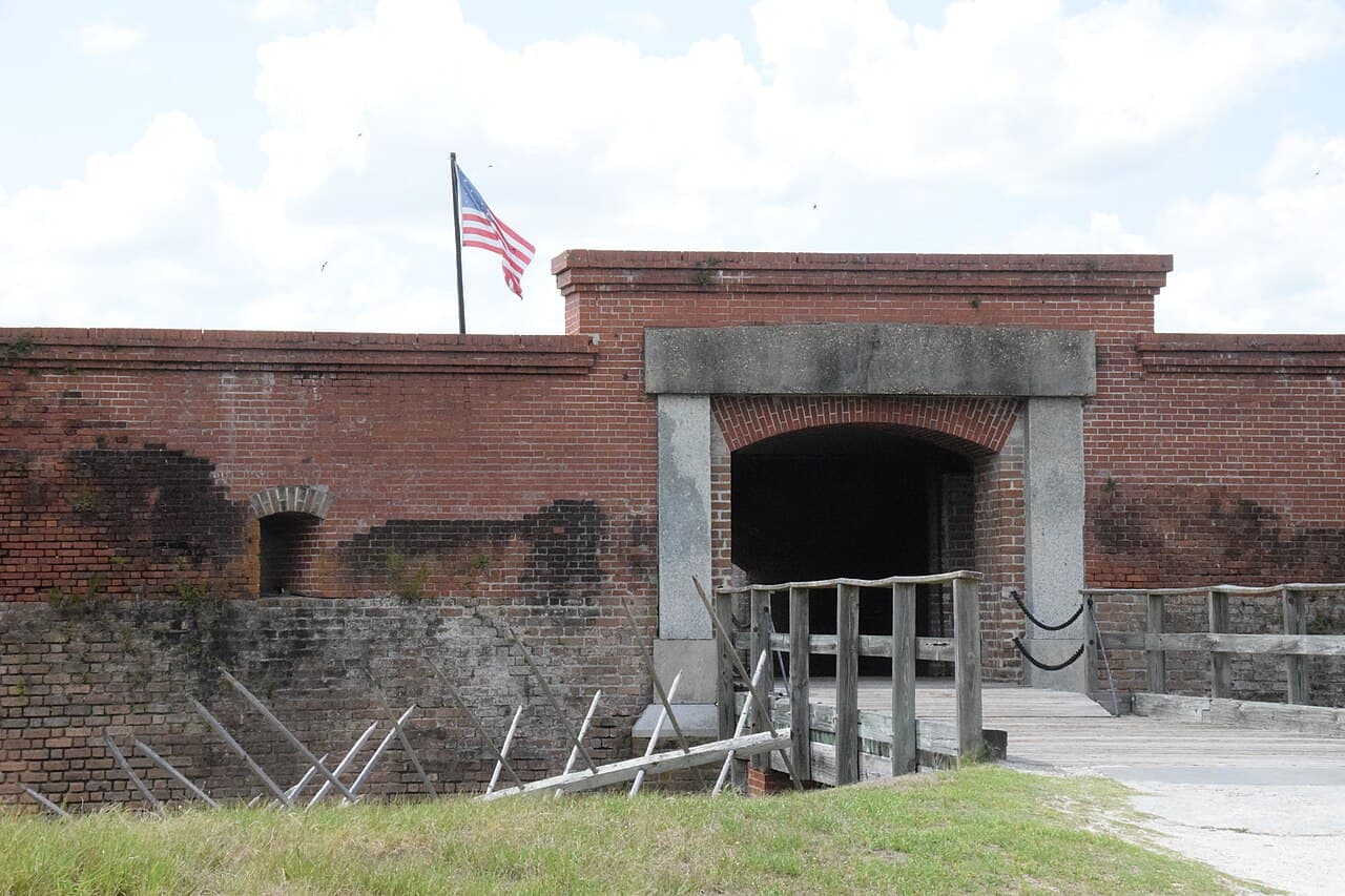 The red-brick entrance and sally port of Fort Clinch at Fort Clinch State Park, a US flag flying above the ramparts, a wooden drawbridge and angled defensive spikes below