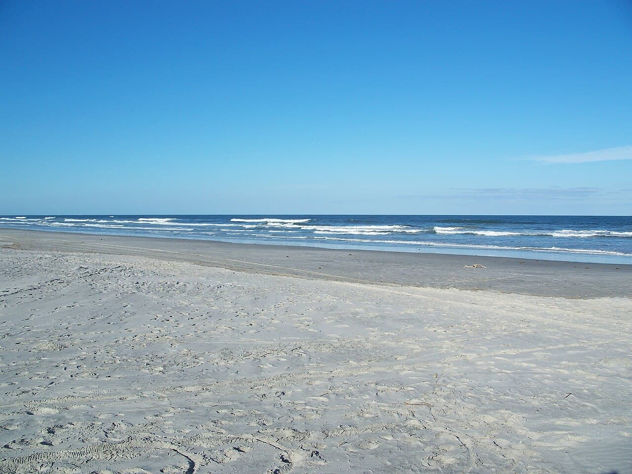 A wide, near-empty sandy Atlantic beach at Little Talbot Island State Park, gentle surf rolling in under a clear blue sky